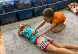 Zajęcia w grupie 1. Cłopiec próbuje obrócić dziewczynkę leżącą na brzuchu na plecy.